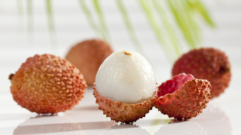 Whole and cracked open lychee fruit on a white glass surface