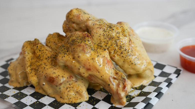 Lemon pepper wings stacked on a checkered paper with dips on the side