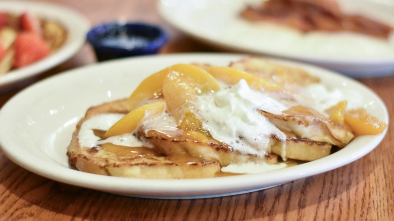 A white plate with French toast, peach topping, and whipped cream
