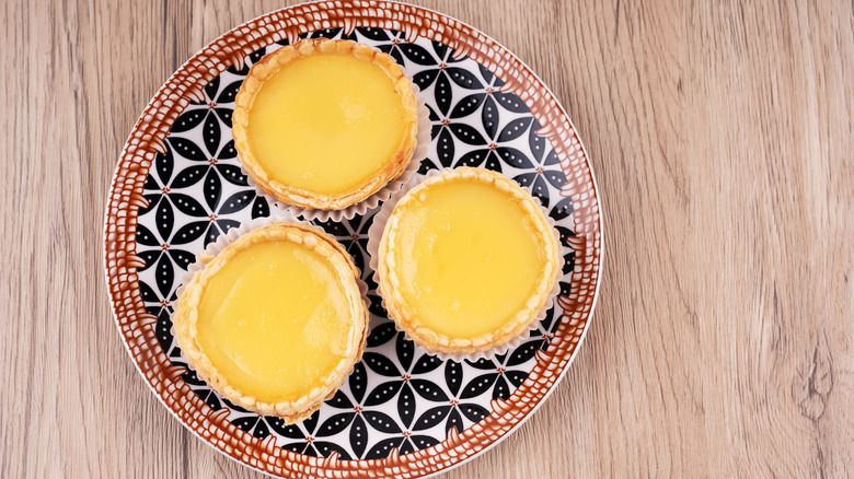 Three Chinese egg tarts on a black and white patterned plate with a red and white border on a wood table
