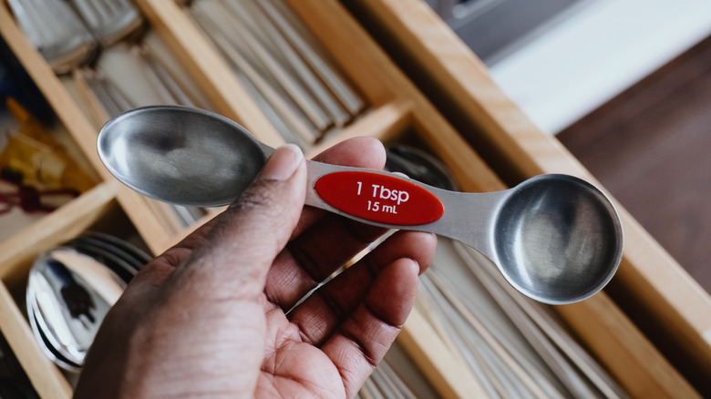 A person holding a tablespoon measuring spoon