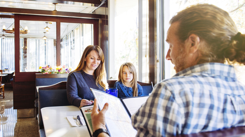 A mom, dad, and daughter sitting in a booth at a restaurant looking at menus