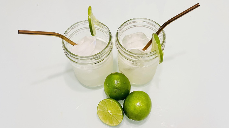 Two margaritas with lime wheel garnishes and fresh limes on the side