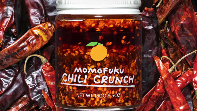 A jar of Momofuku Chili Crunch against a background of dried chili peppers