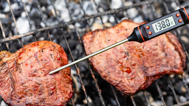 A perons checking the temperature of grilled steaks with a digital meat thermometer