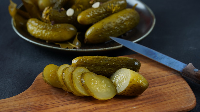 Sliced pickles are picturted on a cutting board with more whole pickles in a bowl in the background.