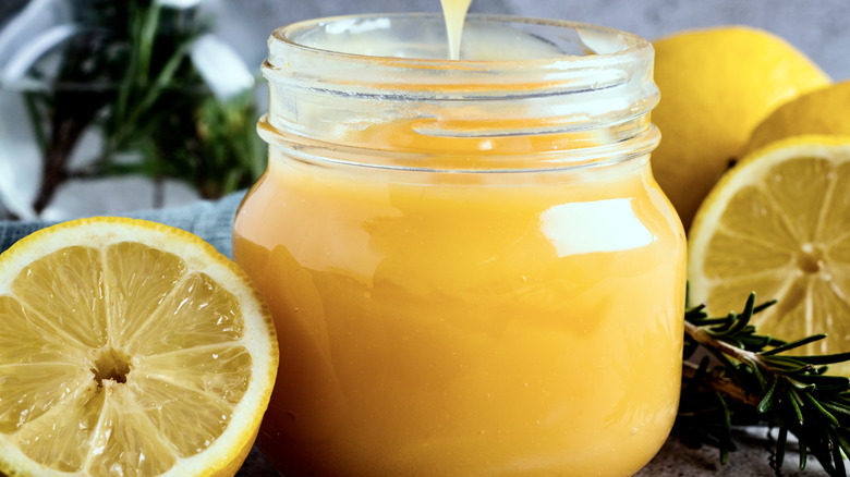 Lemons are arranged around a jar of bright yellow lemon curd.