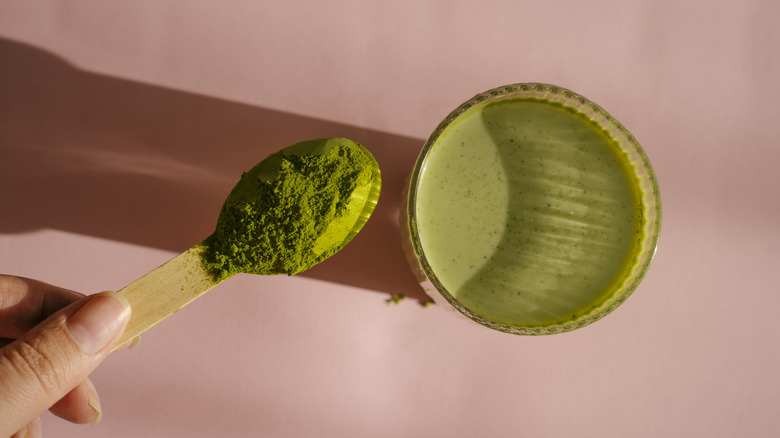 Glass of matcha with matcha powder on pink background