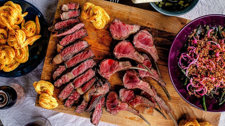 Sliced medium rare lamb steak and lamb chops on wooden cutting board