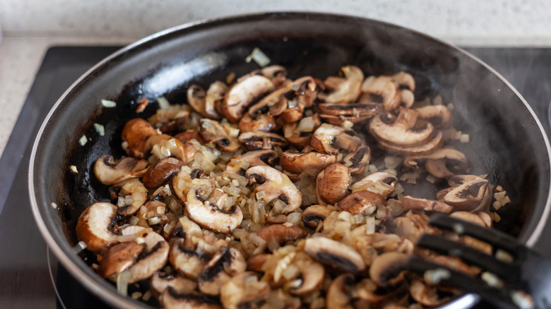 Mushrooms and onions sautéeing in a pan on the stove