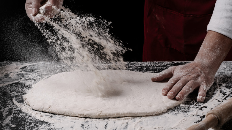 hand tossing flour onto flattened pizza dough