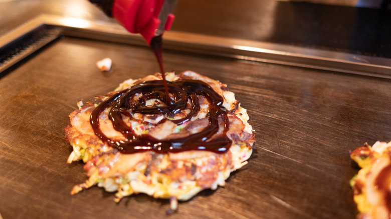 sauce being drizzled on okonomiyaki