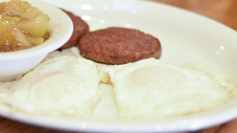 A white plate with fried eggs, sausage patties, and fried apples