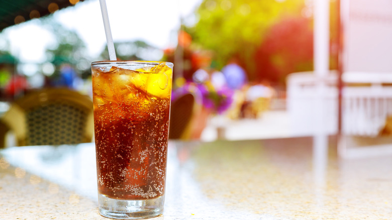 a glass of soda with a straw on an outdoor table