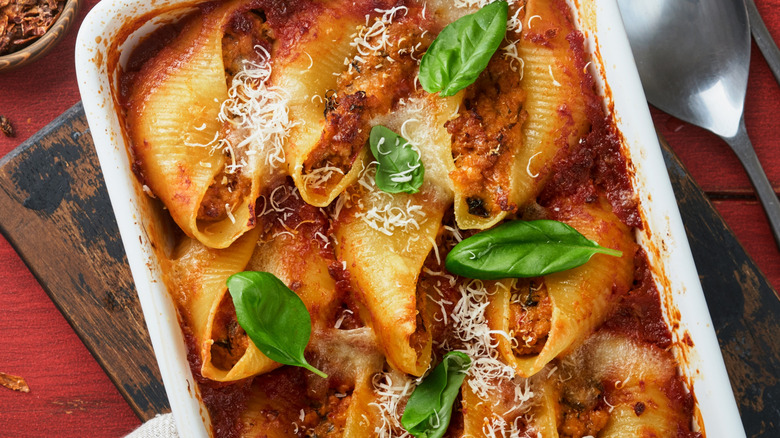 A white tray of stuffed shells with basil and grated Parmesan on top