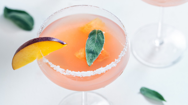 A peach cocktail in a coupe glass with a peach garnish