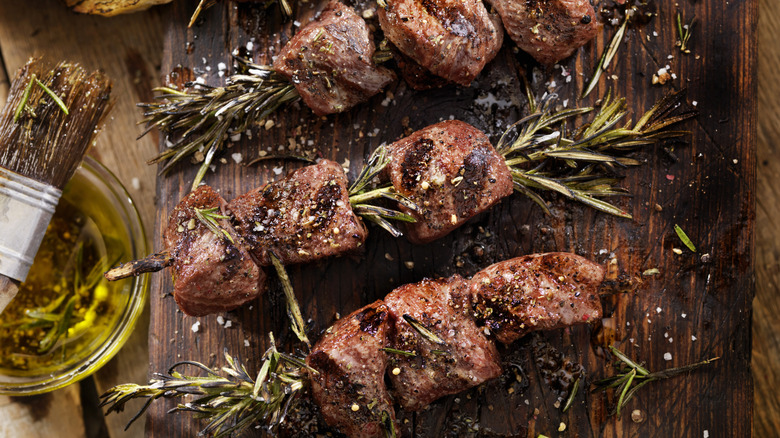 Steak kabobs are skewered with rosemary and presented on a cutting board.