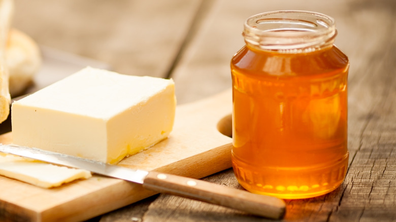 a jar of honey next to a slab of butter with a knife