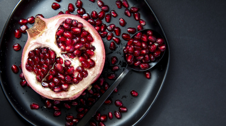 Half pomegranate and seeds on a black plate