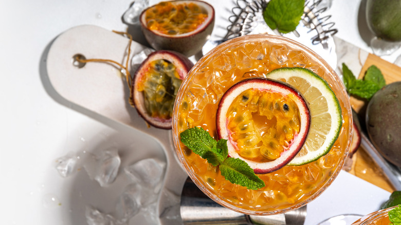 A orange cocktail in a coupe glass with a passion fruit garnish