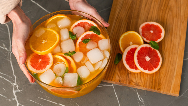 Hands place punch bowl with ice and fruit slices on table