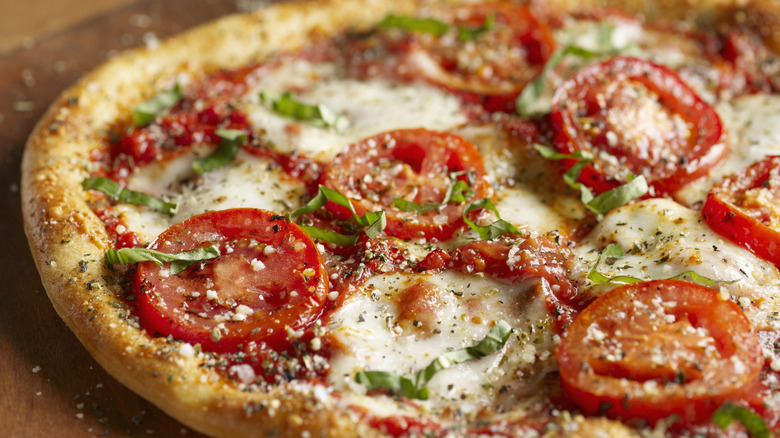 A pizza with tomato slices and basil on top
