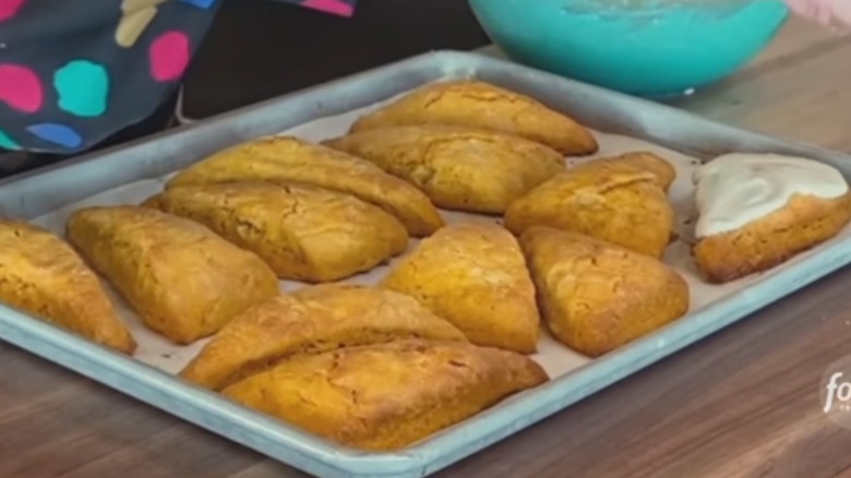 A tray of baked pumpkin scones with one on the right fully iced