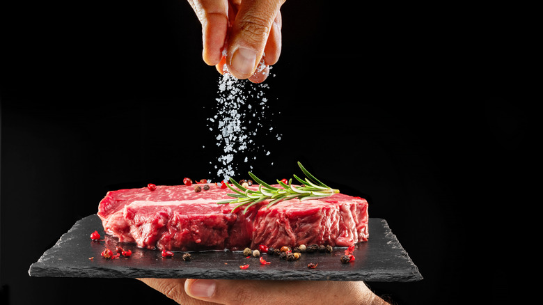 A person salting a raw steak on a plate
