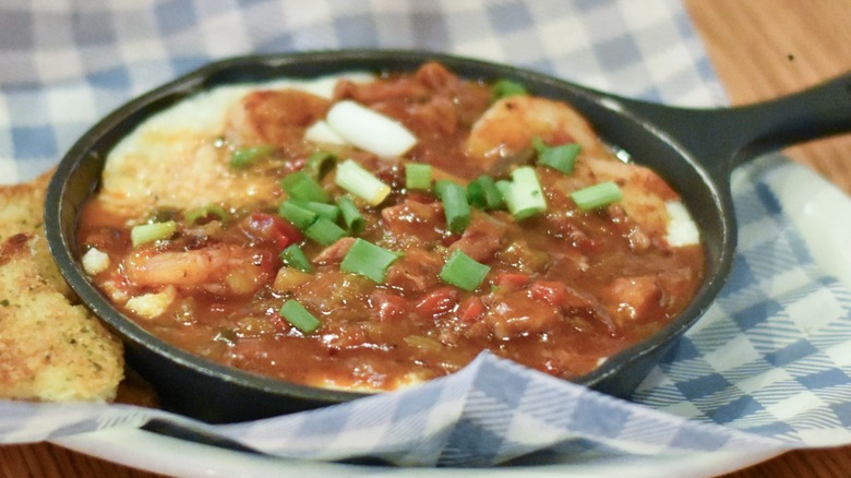 A black cast iron skillet with shrimp, grits, and sauce with green onions on top