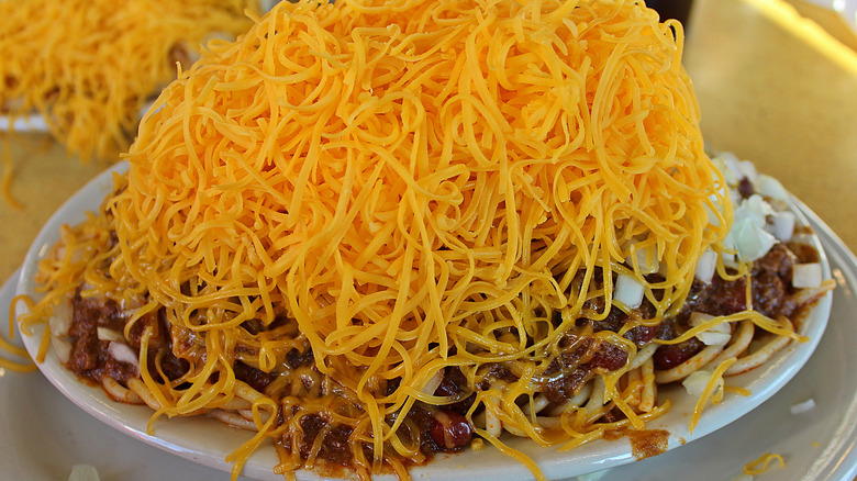 A plate of spaghetti topped with Cincinnati chili and cheddar cheese.