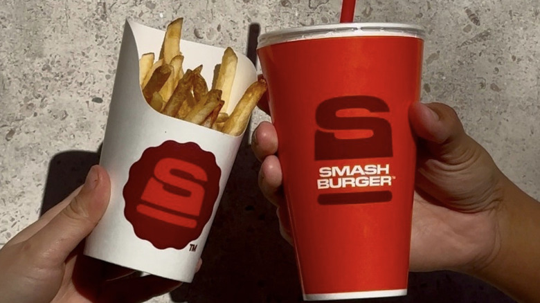 Hands holding a drink and fries from Smashburger with the new logo design