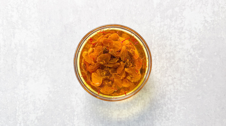 Golden raisins and saffron threads soaking in water in glass bowl
