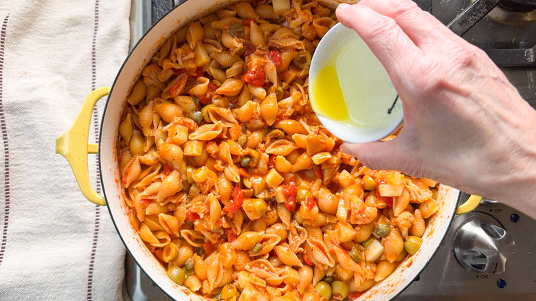 Drizzling olive oil over Spanish romesco-y tuna casserole in pot on stovetop