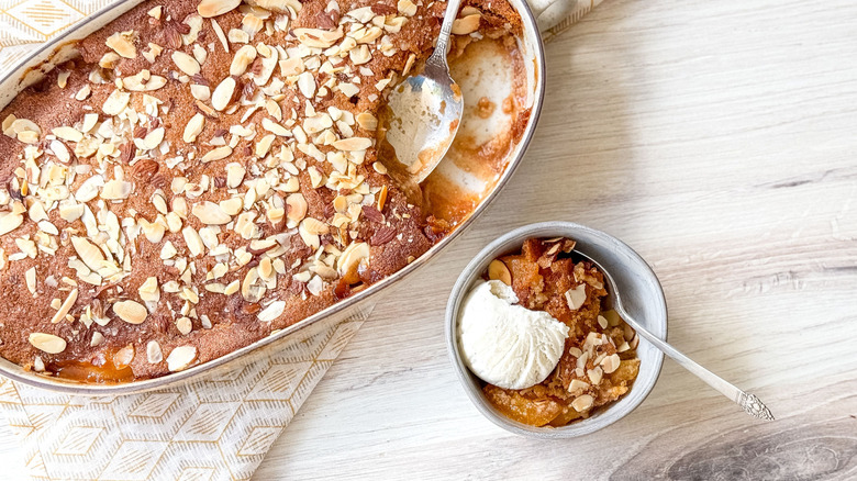 Gluten-free peach cobbler in baking dish and serving bowl with vanilla ice cream