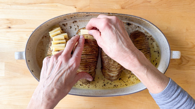 Putting slices of Jarlsberg cheese in Hasselback potatoes in casserole dish