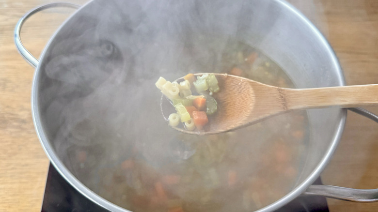 wooden spoon with pasta and chopped vegetables hovering over a metal pot