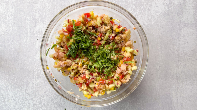 Sliced basil and mint on top of panzanella salad in glass bowl