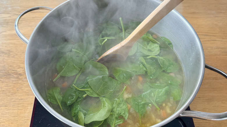 spinach in a metal pot with broth and a wooden spoon