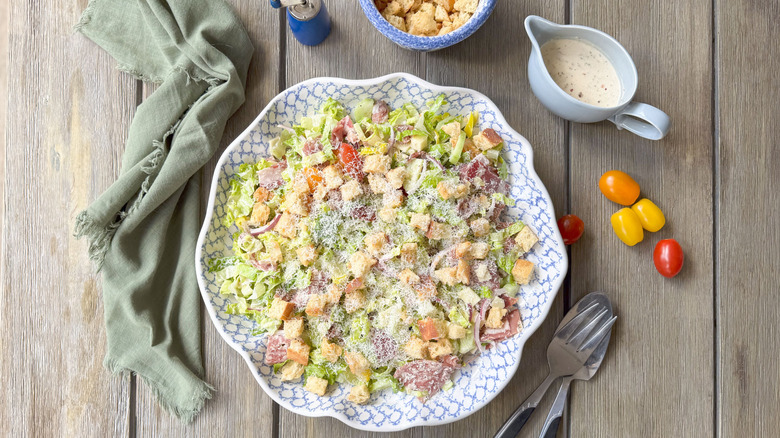 Italian deli grinder salad in large serving bowl with croutons, dressing and tomatoes on the side