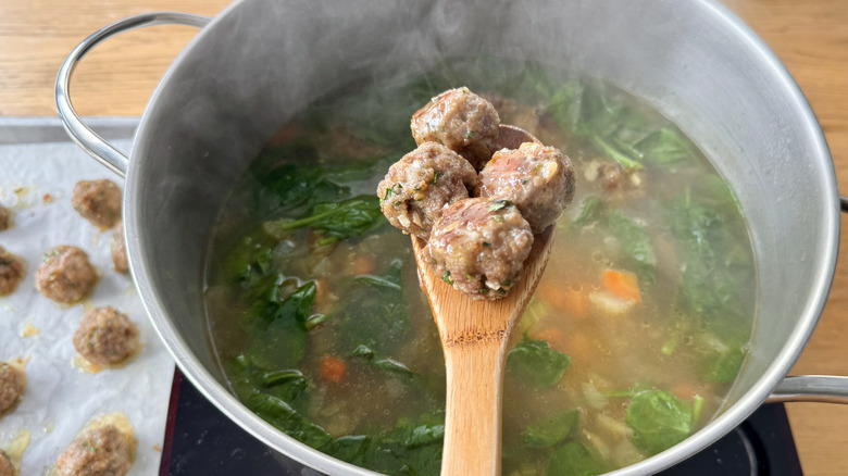 wooden spoon with meatballs hovering over a metal pot