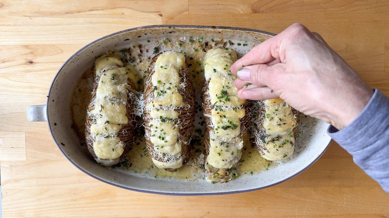 Sprinkling herbs on extra cheesy Hasselback potatoes