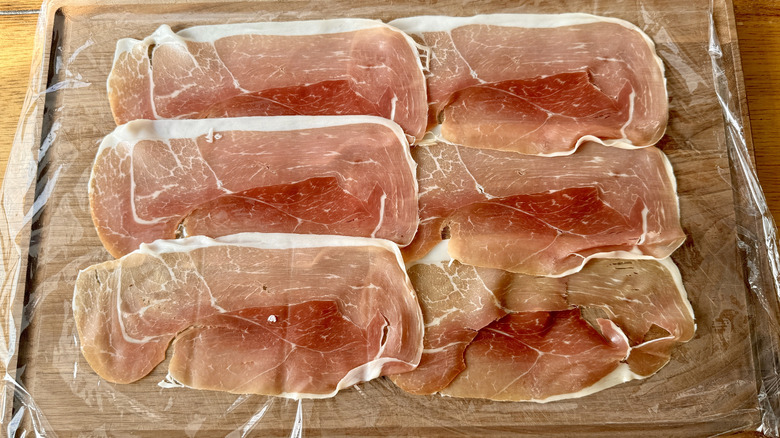 sliced prosciutto on plastic wrap