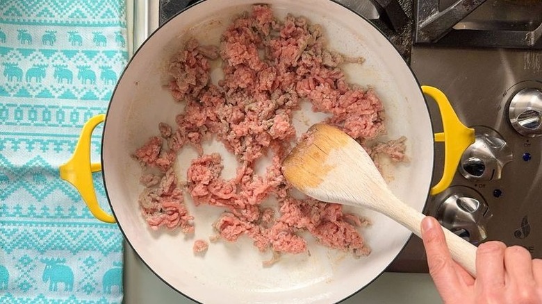 Browning ground turkey in pot on stove with wooden spoon
