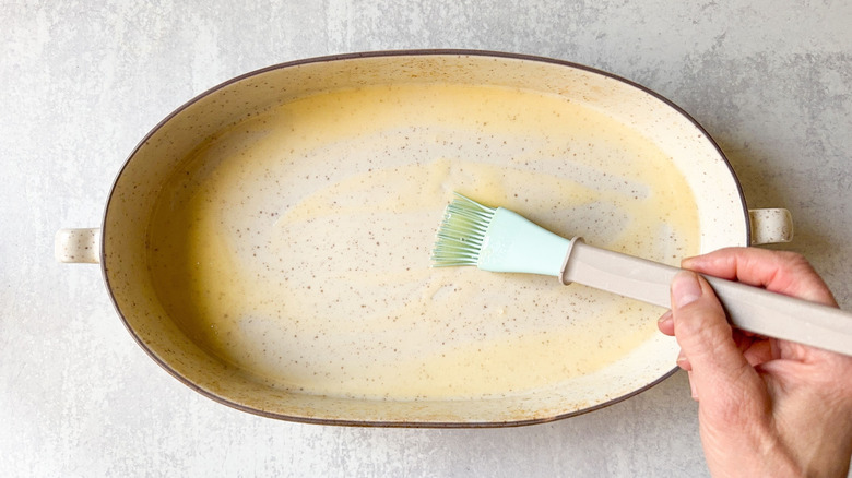 Brushing the inside of an oblong baking dish with melted butter