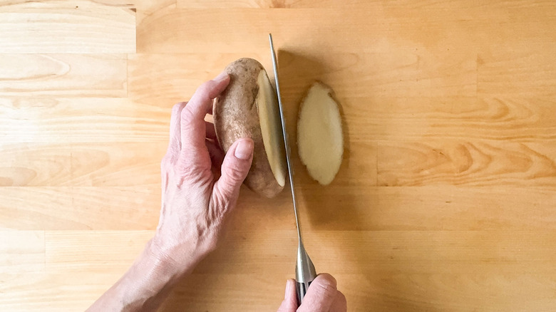 Cutting a slice from a potato on cutting board