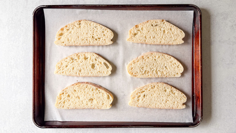 Parchment-lined baking sheet with slices of ciabatta bread
