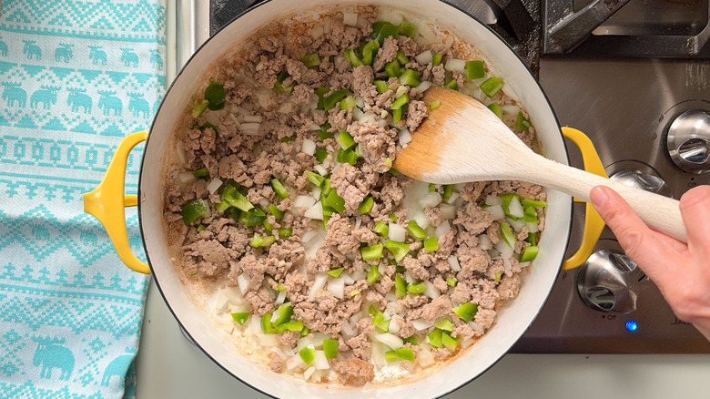 Sauteeing ground turkey, onion, green bell pepper, and garlic in pot on stove with wooden spoon