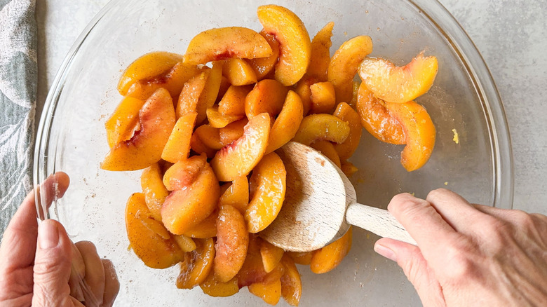 Stirring peach slices with sugar, cornstarch, and cinnamon in glass bowl with wooden spoon