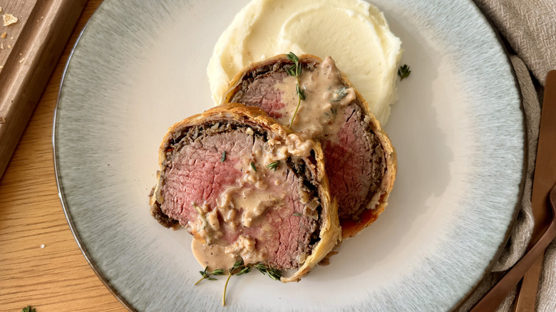 sliced beef wellington with sauce and mashed potatoes