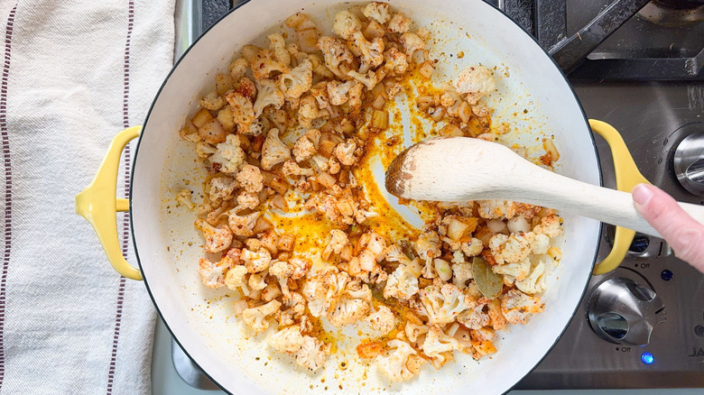 Sautéing cauliflower, onion and seasonings with wooden spoon in pot on stovetop